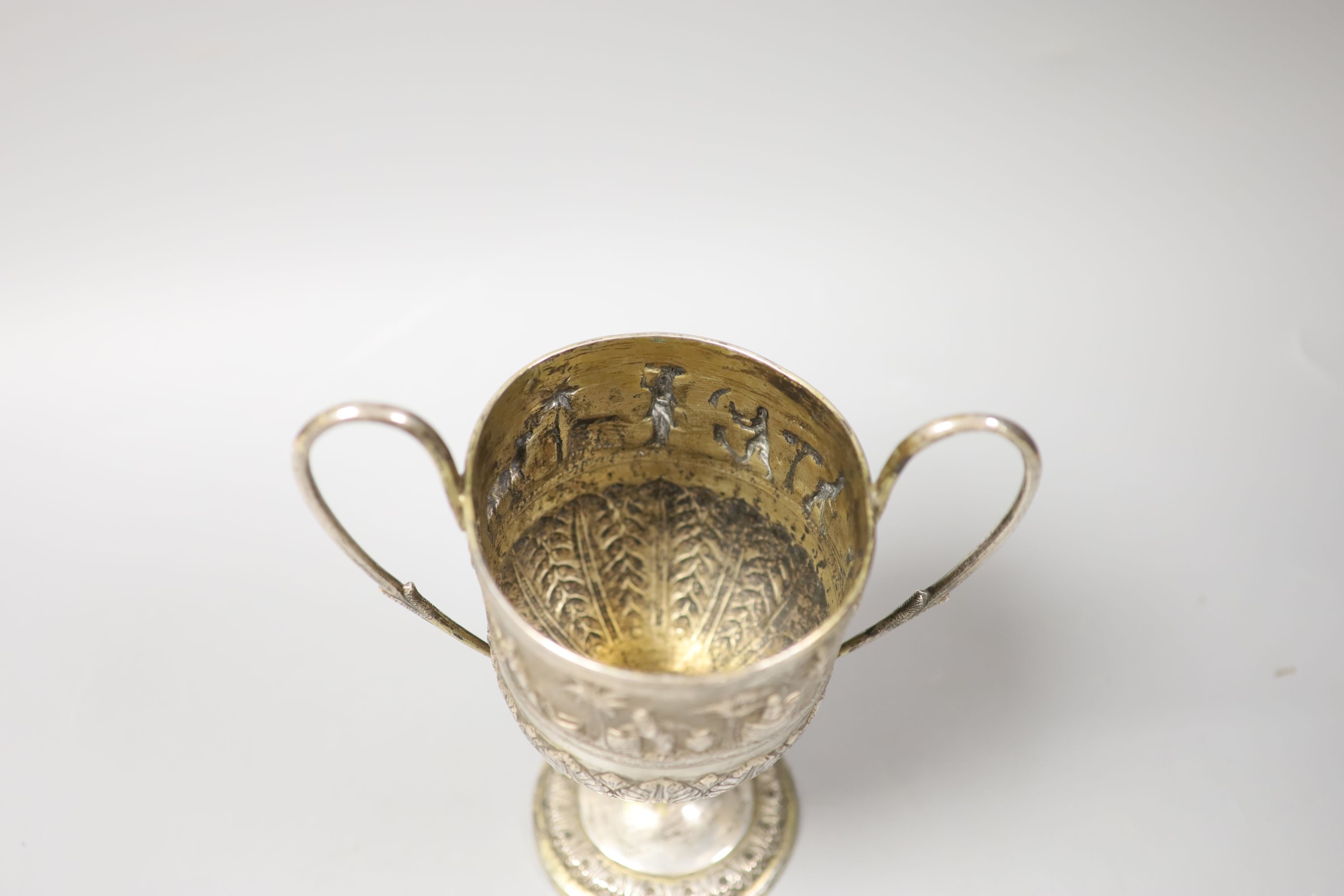 An embossed Indian white metal two handled pedestal trophy cup, height 22.2cm, 12.5oz.